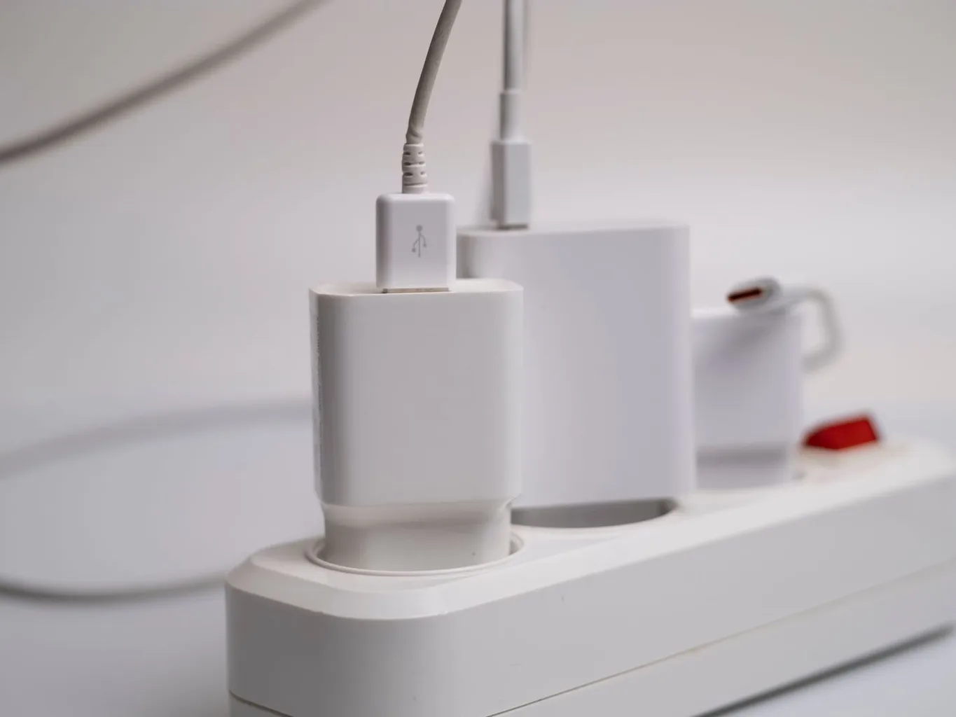 White chargers plugged into a power strip with a red switch, a cord looping across a light surface